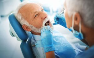 older man sitting in dental chair getting his teeth examined by dentist restorative solutions Columbia South Carolina